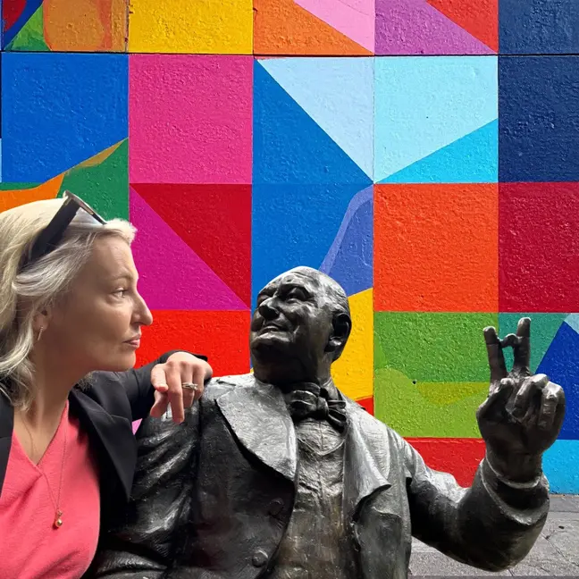 Elise beside a sculpture against a vivid geometric mural
